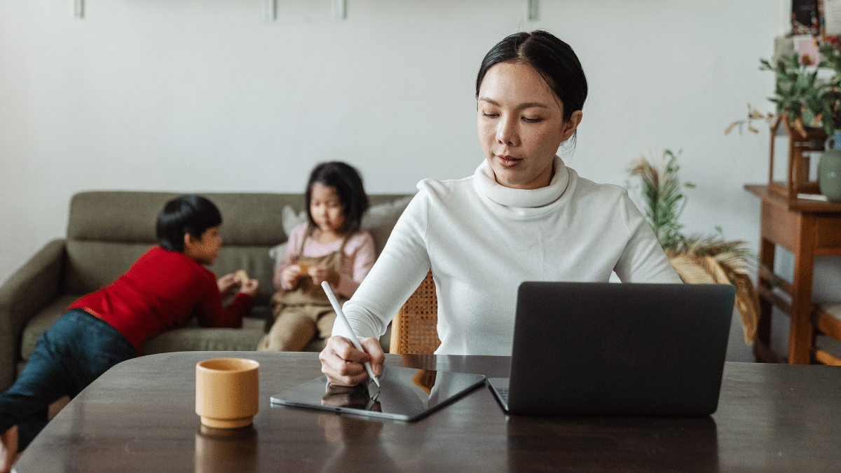A woman working remotely while her kids hang out on the sofa